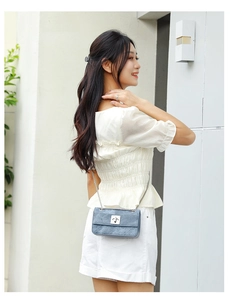 Detail of blue denim quilted crossbody bag featuring silver twist lock and metal chain strap