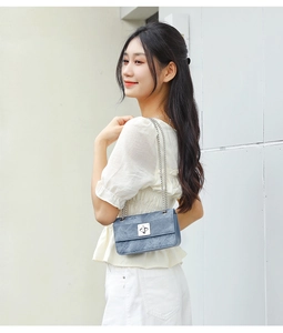 Blue denim crossbody bag with silver chain strap shown on model against white wall