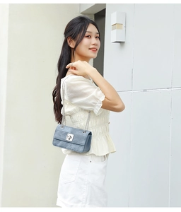 Detail of light blue denim quilted texture and silver chain strap on a mini flap bag