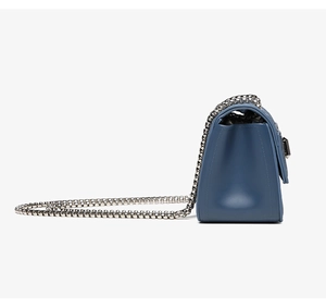 Side view of blue quilted crossbody bag with silver chain strap and metal hardware