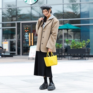 Femme à la mode portant un sac cabas en PVC jaune ajouré dans un décor de rue urbain moderne