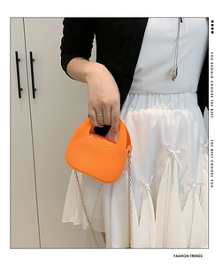 Close-up of vibrant orange glossy crossbody bag with sleek metallic gold chain strap