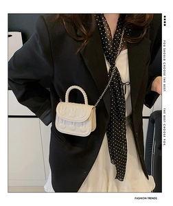 Detail view of cream crossbody bag featuring embossed rabbit pattern and pearl handle