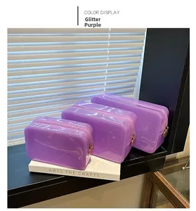 Three-piece purple glitter makeup bag set with gold heart zippers on a windowsill