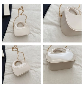 Detail view of cream patent leather evening bag with round handle and gold chain strap