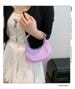 Detail of a purple crescent handbag with glossy finish worn by a model in a trendy outfit