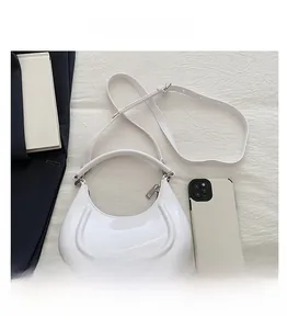 Top-down view of white crescent moon bag on fabric next to black suit and phone