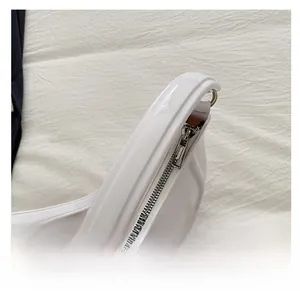Close-up of white patent leather crescent bag featuring silver metal zipper and stitching