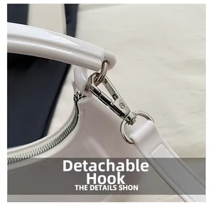 Close-up detail of silver detachable metal hook and zipper on white glossy crescent bag