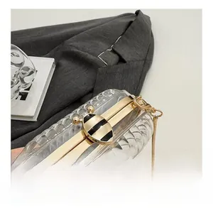 Detail view of a golden bee clasp on a transparent acrylic evening bag with metal chain