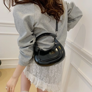 Glossy black crescent handbag with mirror finish, shown styled as a crossbody bag