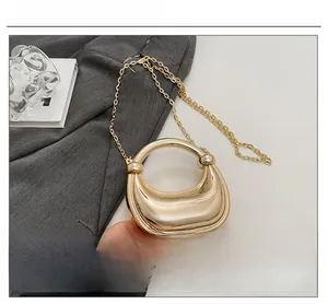 Detailaufnahme der glänzenden goldenen Sichltasche mit poliertem Metallgriff und Kette