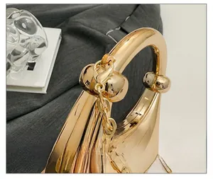 Detail der champagnergoldenen Metallic-Abendtasche mit gebogenem Griff und Kettenriemen