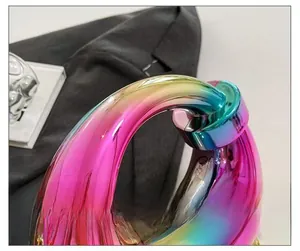 Detail of premium acrylic evening bag featuring iridescent gradient finish and ring handle