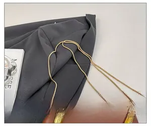 Detail van een bruine leren tas met gouden slangenketting en ovaal metalen handvat