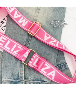 Adjustable pink woven shoulder strap with white letter pattern and gold buckle detail