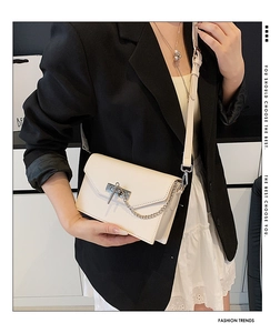 Modern cream crossbody bag with silver lock shown on a model in a black blazer