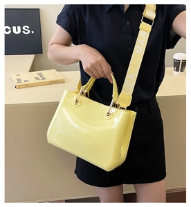 Detail of glossy yellow handbag with top handle and lettered wide shoulder strap