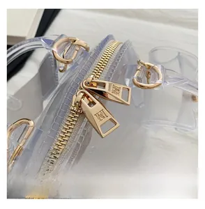 Macro detail of transparent PVC jelly bag featuring a gold zipper with engraved M logo