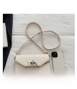 Detail view of cream mini crossbody bag with silver lock and smartphone for scale