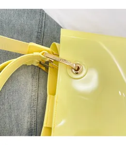 Detailed close-up of golden metal hooks and brand logo on a yellow patent leather handbag