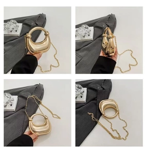 Macro detail of glossy gold acrylic laser dumpling bag with metallic chain and handle
