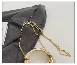 Detailed close-up of polished gold chain strap with circular metal handle on textured fabric