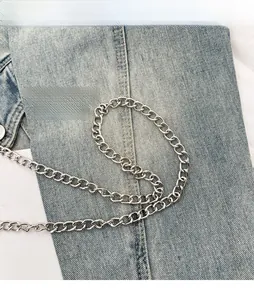 Détail d'une bandoulière en chaîne argentée avec maillons ovales sur denim