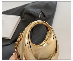 Close-up of golden oval hardshell handbag featuring a round ergonomic handle and chain