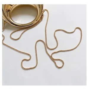 Elegant gold round handle and delicate metallic chain strap on white textured background