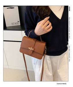 Detail of brown lychee texture leather shoulder bag with golden metal bar lock closure