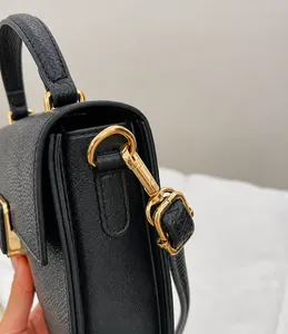Close-up of golden metal D-ring and spring hook on black pebble leather bag
