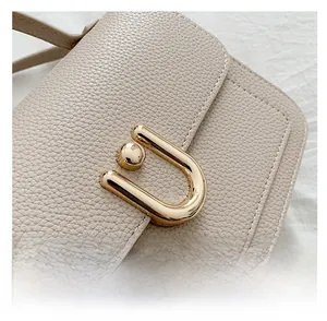 Close-up of beige lychee grain leather handbag with golden U-shaped metal lock