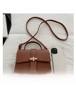 Detail view of brown lychee grain leather mini bag with golden cross buckle and smartphone