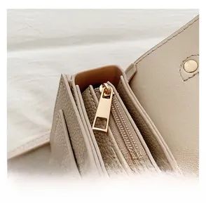 Close-up of beige lychee grain leather handbag with gold rectangular zipper detail