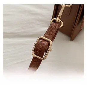 Detail of adjustable brown leather strap with lychee texture and gold metal hardware