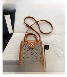 Detail view of the brown monogram crossbody bag with golden hardware and phone for scale
