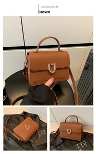Detail view of brown lychee leather handbag with golden U-shaped buckle and crossbody strap