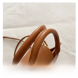 Close-up of caramel brown leather handbag showing cylindrical handles and gold metal rings