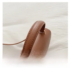 Detail view of the arched leather handle and metal hardware on the caramel crossbody bag