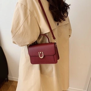 Elegant wine red lychee pattern handbag with golden U-shaped buckle on beige trench coat