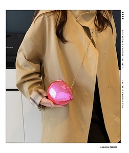 Close-up of pink mirror egg-shaped evening bag with gold chain strap on trench coat