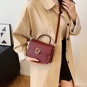 Elegant wine red leather handbag with gold U-shaped hardware shown on a beige trench coat