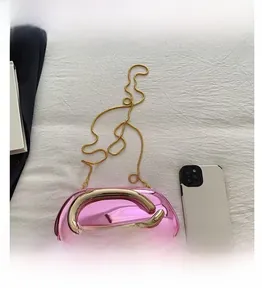 Détail macro de la pochette en acrylique rose brillant avec poignée serpent dorée