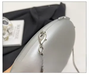 Detail showing polished silver metal lobster clasp and sleek snake chain on a clutch bag