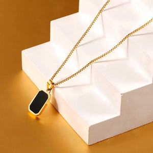 Minimalistische Goldkette mit schwarzem rechteckigem Anhänger auf weißem Steinstufen