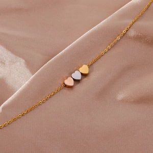 Gros plan de pendentifs en forme de cœur tricolore or, argent et or rose sur fond de soie