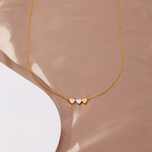 Vue détaillée de trois pendentifs cœur minimalistes en finitions or rose, argent et doré