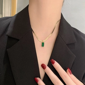 Détail d'un collier chaîne serpent dorée avec pendentif gemme verte porté par un mannequin