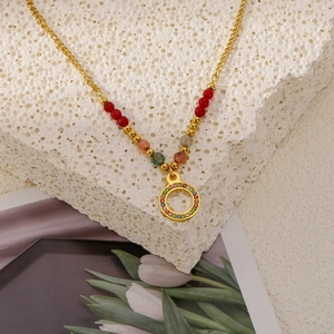 Elegante goldene Titanhalskette mit bunten Perlen und rundem Kristallanhänger auf Stein